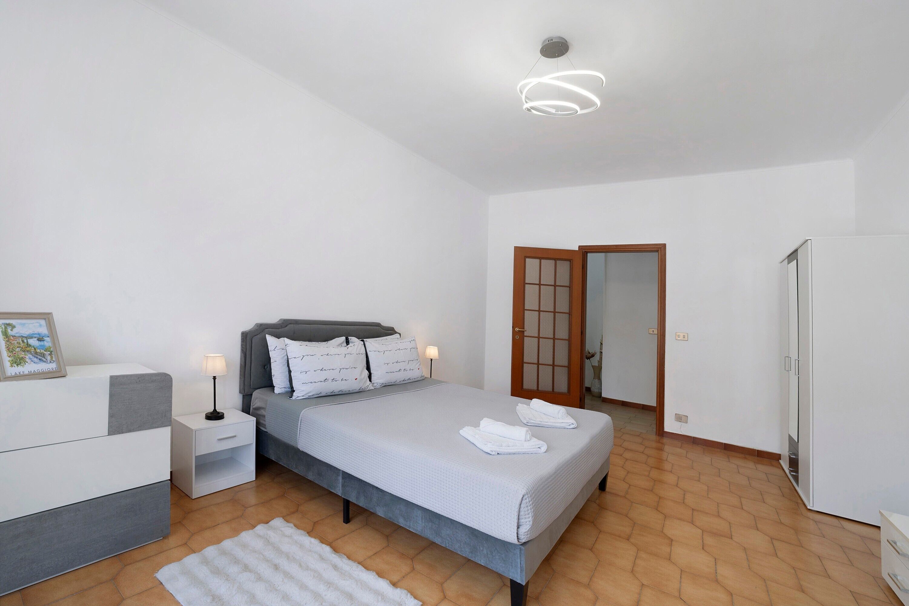 Ein Schlafzimmer mit Bett, Nachttischen, einem Bildrahmen, einer Tür und einem Kleiderschrank.