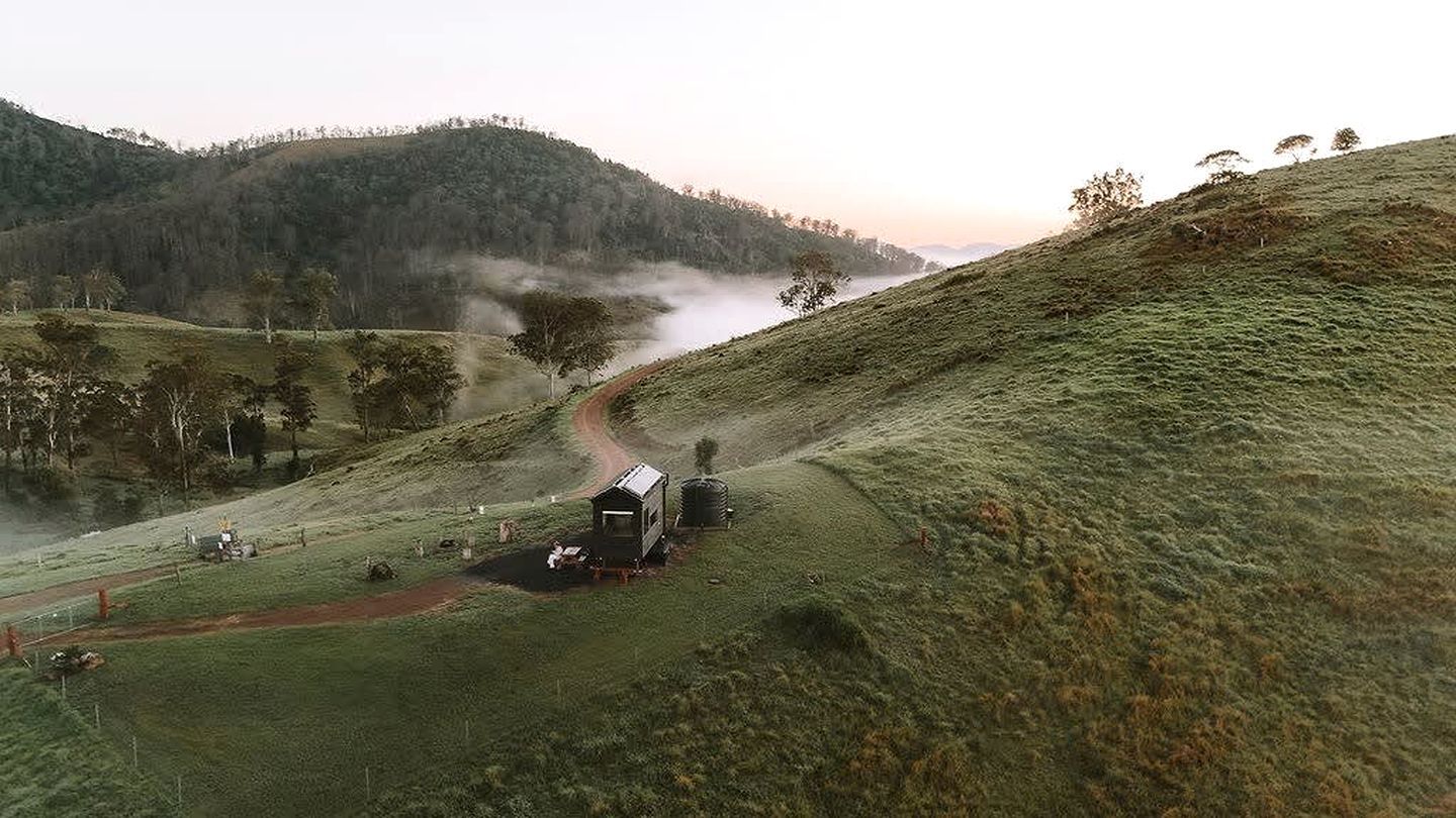 A rural landscape with a small building, a dirt path, and a body of water in the distance.