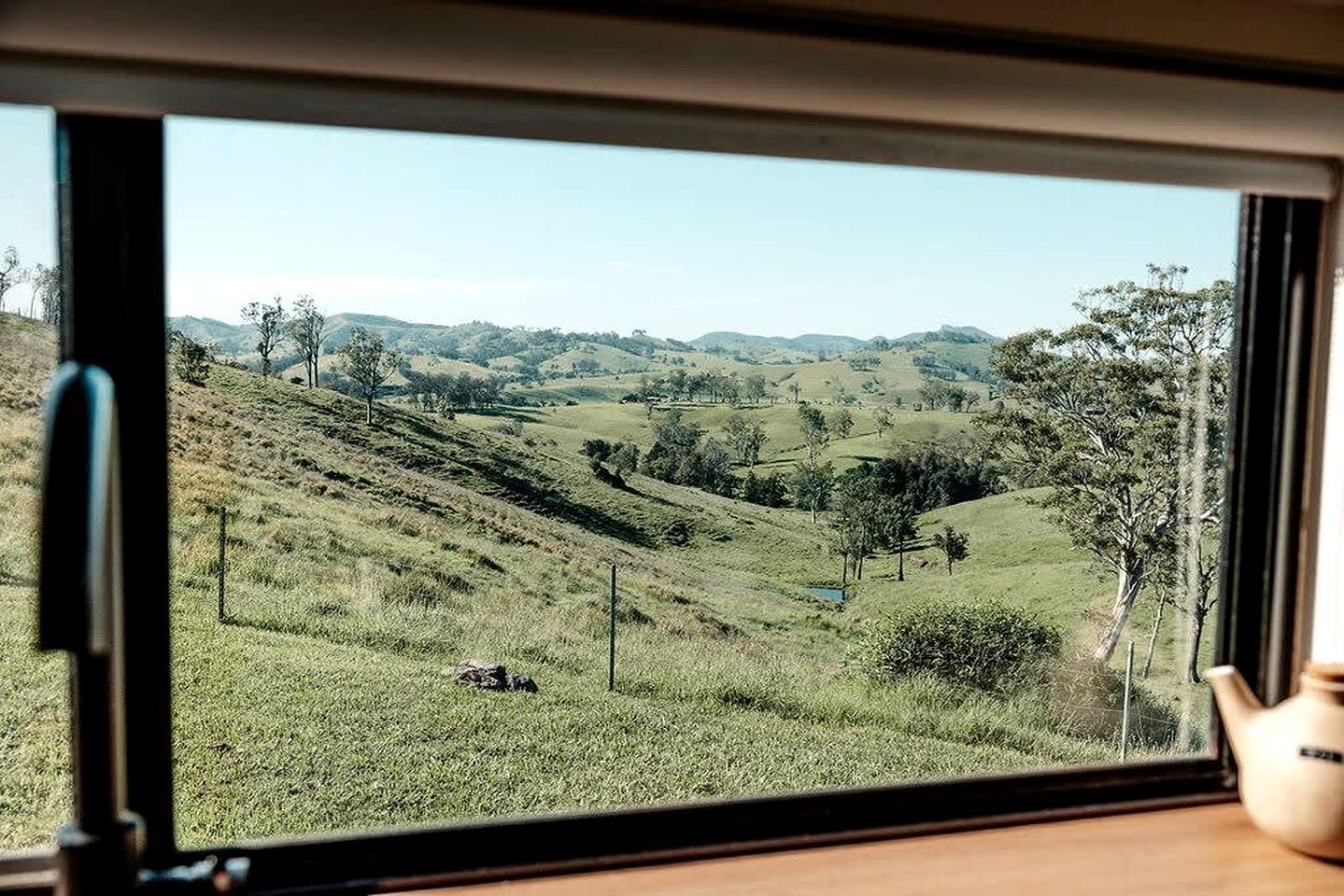 A view through a window of a rural landscape with rolling hills, trees, and a clear sky.