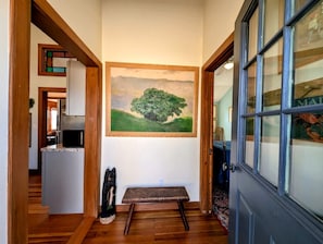A hallway with a painting of a tree, a bench, and a door with a window. - Picturesque Waterfront Cottage with Waterfall Views, Fireplace & Deck, Near Acadia National Park in Gouldsboro, Maine (Gouldsboro)