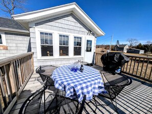 Eine Terrasse mit Esstisch, Grill und einem Haus im Hintergrund.