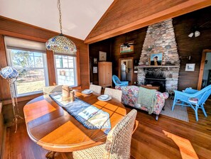 Ein gemütliches Interieur mit Kamin aus Stein, Holzwänden und einem Essbereich mit Korbmöbeln.