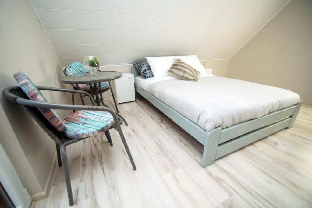 A small, single-room apartment with a bed, a chair, a small table, and a nightstand.