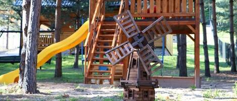 A playground with a windmill structure, a slide, and a wooden playhouse.