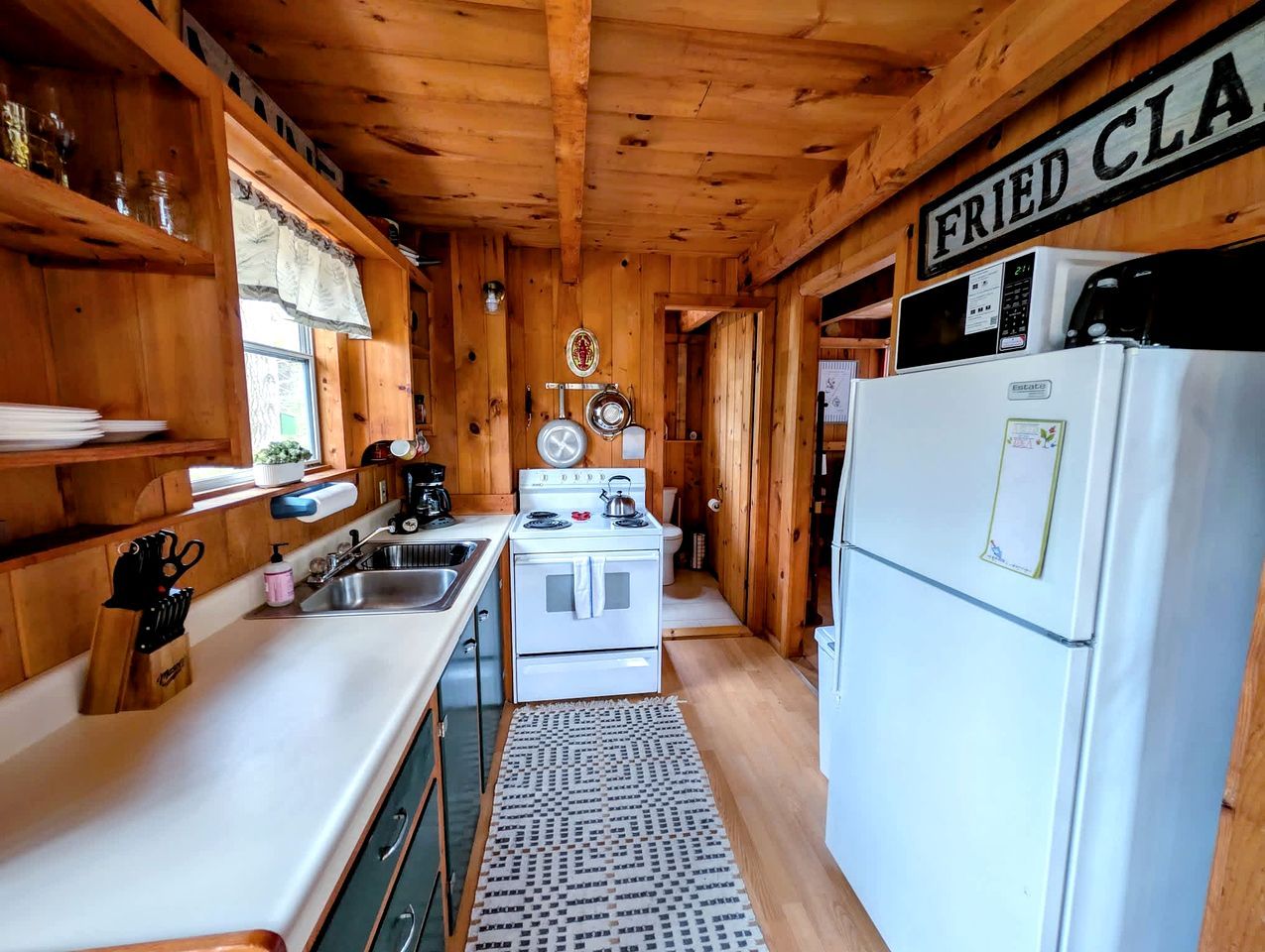 A kitchen with wooden walls, a stove, a sink, and a refrigerator.