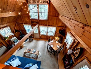 A wooden cabin interior with a dining area, a sofa, and a sign reading 'MT. DESERT ISLAND'. - Charming Cabin with Fireplace Near Scenic Trails in Mount Desert, Maine (Mount Desert)