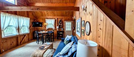 A cozy cabin interior with a wooden ceiling, a sofa, a dining table, and a fireplace.
