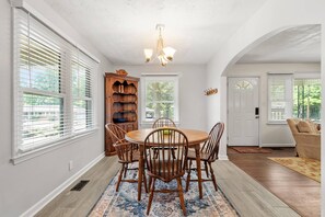 A dining area with a round table, wooden chairs, a chandelier, and a view of the outdoors through large windows. - New- Minutes from Atl Attractions, Hiking, Beltline, Backyard, Grill,  Pet Friendly (Atlanta)