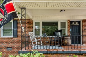 A brick house with a porch, a flag, and outdoor furniture. - New- Minutes from Atl Attractions, Hiking, Beltline, Backyard, Grill,  Pet Friendly (Atlanta)