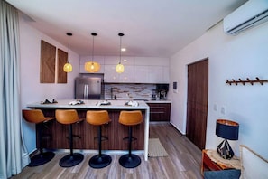 A modern kitchen with a central island, bar stools, pendant lights, and a coffee machine. - Enjoy Tulum from Athara by HEUSHAVEN, a modern apartment in La Veleta, next to Central Park Lagunas. Ideal for couples or relaxed getaways, with a private pool, equipped kitchen, WiFi and amenities to unwind after the beach. (Tulum)