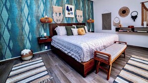 A bedroom with a patterned wall, a bed with a wooden headboard, a bench, a nightstand, and a wall-mounted shelf. - Enjoy Tulum from Athara by HEUSHAVEN, a modern apartment in La Veleta, next to Central Park Lagunas. Ideal for couples or relaxed getaways, with a private pool, equipped kitchen, WiFi and amenities to unwind after the beach. (Tulum)