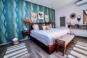 Ein Schlafzimmer mit strukturierten Wandverkleidungen, einem Bett mit Holz-Kopfteil, einer Bank, einem Nachttisch und einem an der Wand montierten Regal.