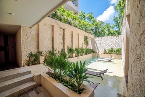 A modern pool area with steps leading down to the water, surrounded by greenery and a stone wall. - Enjoy Tulum from Athara by HEUSHAVEN, a modern apartment in La Veleta, next to Central Park Lagunas. Ideal for couples or relaxed getaways, with a private pool, equipped kitchen, WiFi and amenities to unwind after the beach. (Tulum)