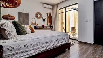 A bedroom with a large bed, a wooden floor, a window with a view, and a door.
