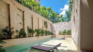 A pool area with lounge chairs, a stone wall, and greenery. - Enjoy Tulum from Athara by HEUSHAVEN, a modern apartment in La Veleta, next to Central Park Lagunas. Ideal for couples or relaxed getaways, with a private pool, equipped kitchen, WiFi and amenities to unwind after the beach. (Tulum)