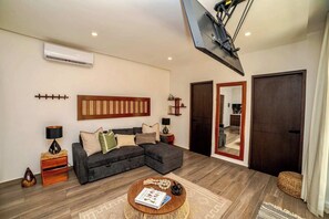 Ein Wohnzimmer mit Ecksofa, Couchtisch, Klimaanlage, Wandfernseher und einem großen Spiegel.