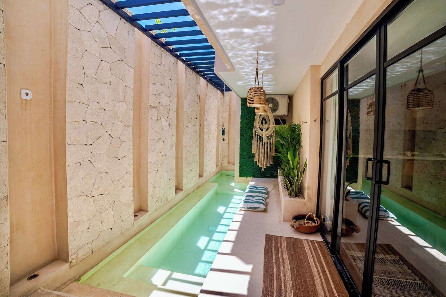 A modern indoor pool area with a glass wall, a blue ceiling, and a green wall with a decorative hanging.