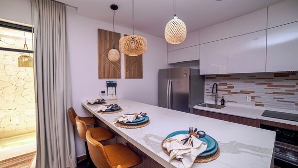 A modern kitchen with a long island, built-in appliances, and a stone wall. - Enjoy Tulum from Athara by HEUSHAVEN, a modern apartment in La Veleta, next to Central Park Lagunas. Ideal for couples or relaxed getaways, with a private pool, equipped kitchen, WiFi and amenities to unwind after the beach. (Tulum)