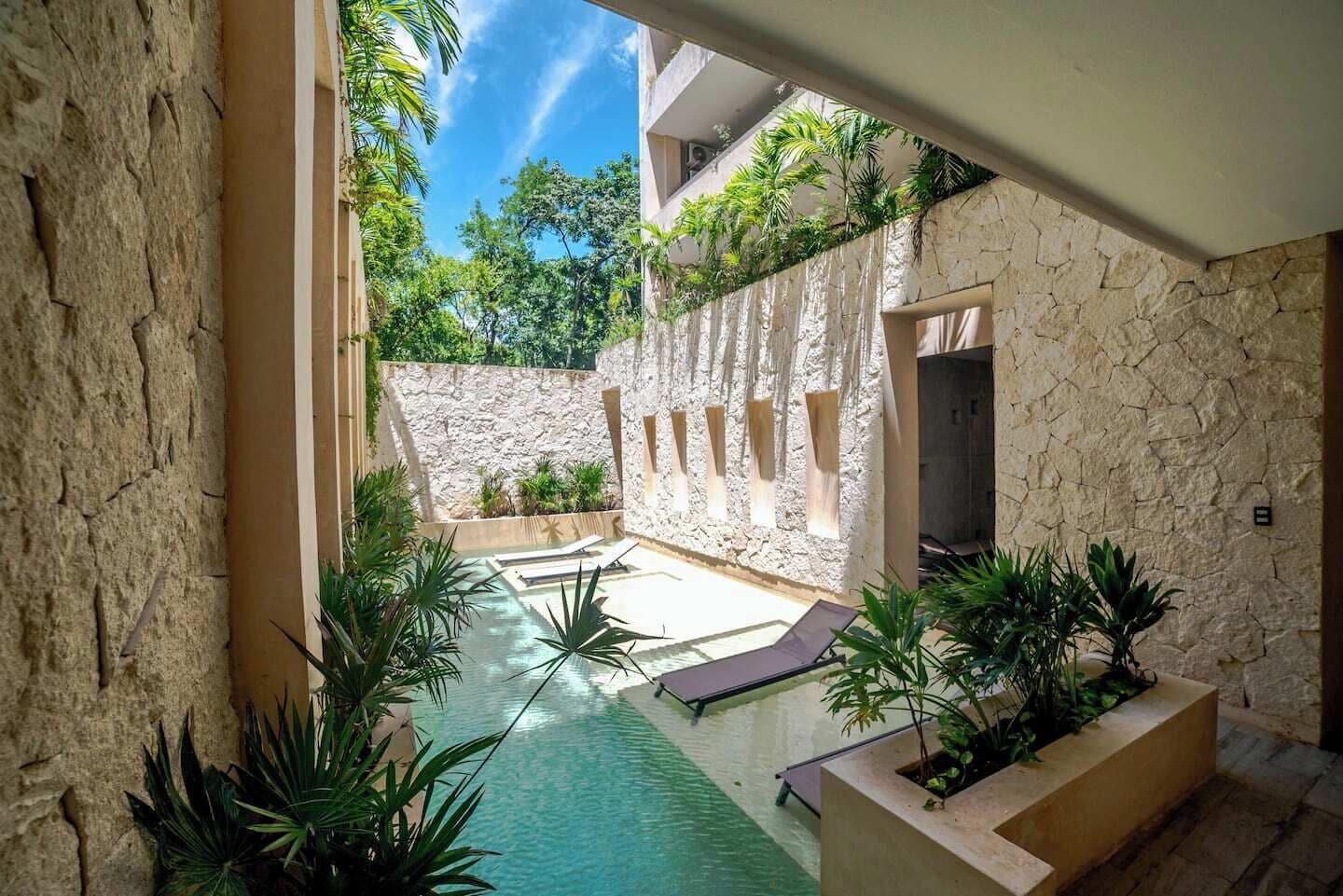A pool area with stone walls, plants, and lounge chairs.
