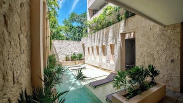 A pool area with stone walls, plants, and lounge chairs.