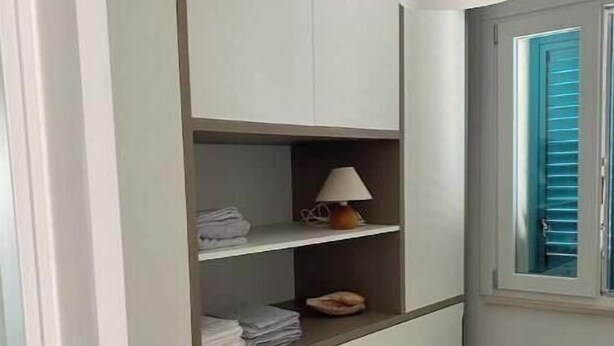 Habitación con escritorio integrado, estanterías, lámpara y ventana con contraventanas azules.