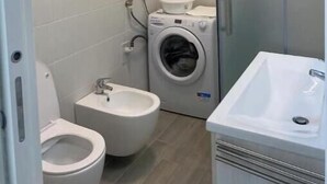 Un baño pequeño con inodoro, bidé, lavadora y lavamanos.