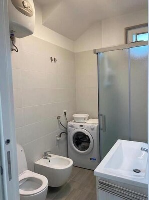 Ein kleines Badezimmer mit Toilette, Bidet, Waschmaschine und Waschbecken.