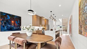 Una cocina moderna con armarios de madera, una isla central, iluminación colgante y un comedor con una mesa redonda y sillas acolchadas.