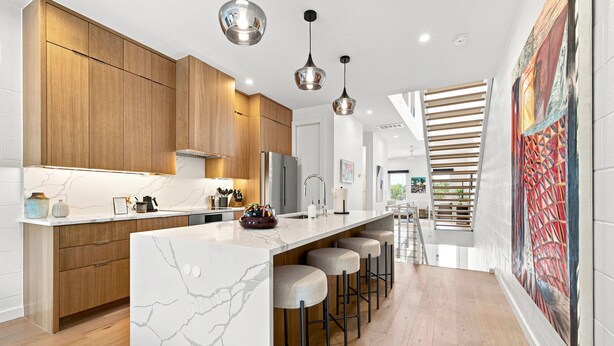 Una cocina moderna con una isla de mármol, armarios de madera y taburetes de bar.