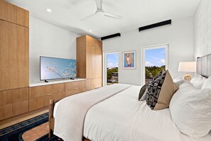 Ein modernes Schlafzimmer mit einem großen Bett, einem Fernseher in einer Wandnische und Blick ins Freie durch ein Fenster.