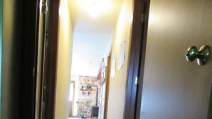 Un pasillo estrecho con puertas de madera, un tapete en el suelo y una pared de piedra al fondo.