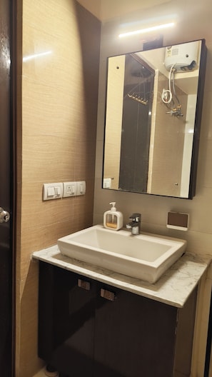 A bathroom with a white sink, a mirror, a towel rack, and a soap dispenser. - Cityscape, Siddha Xanadu, Newtown: Gym, pool, restaurant, garden, 24/7 security. (Kolkata)