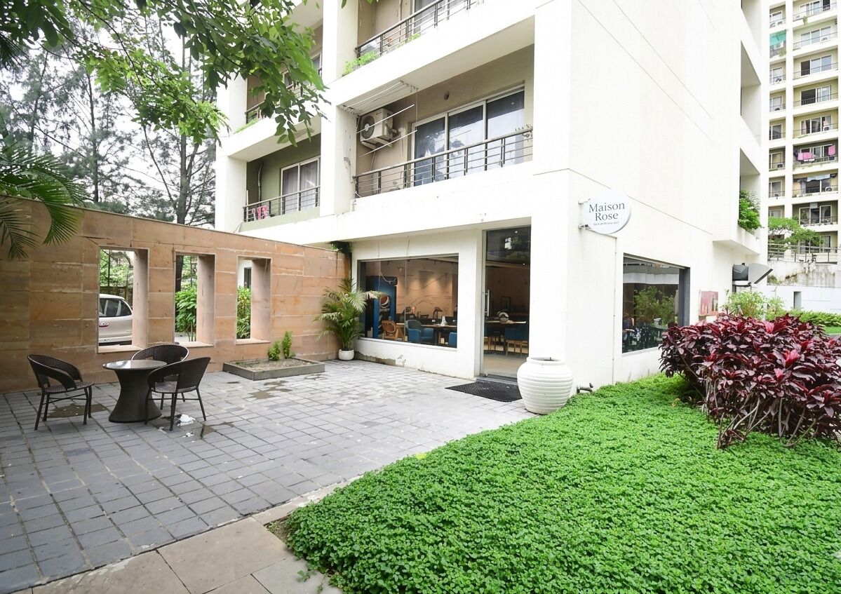 A multi-story building with a restaurant on the ground floor, outdoor seating, and a well-maintained garden area.