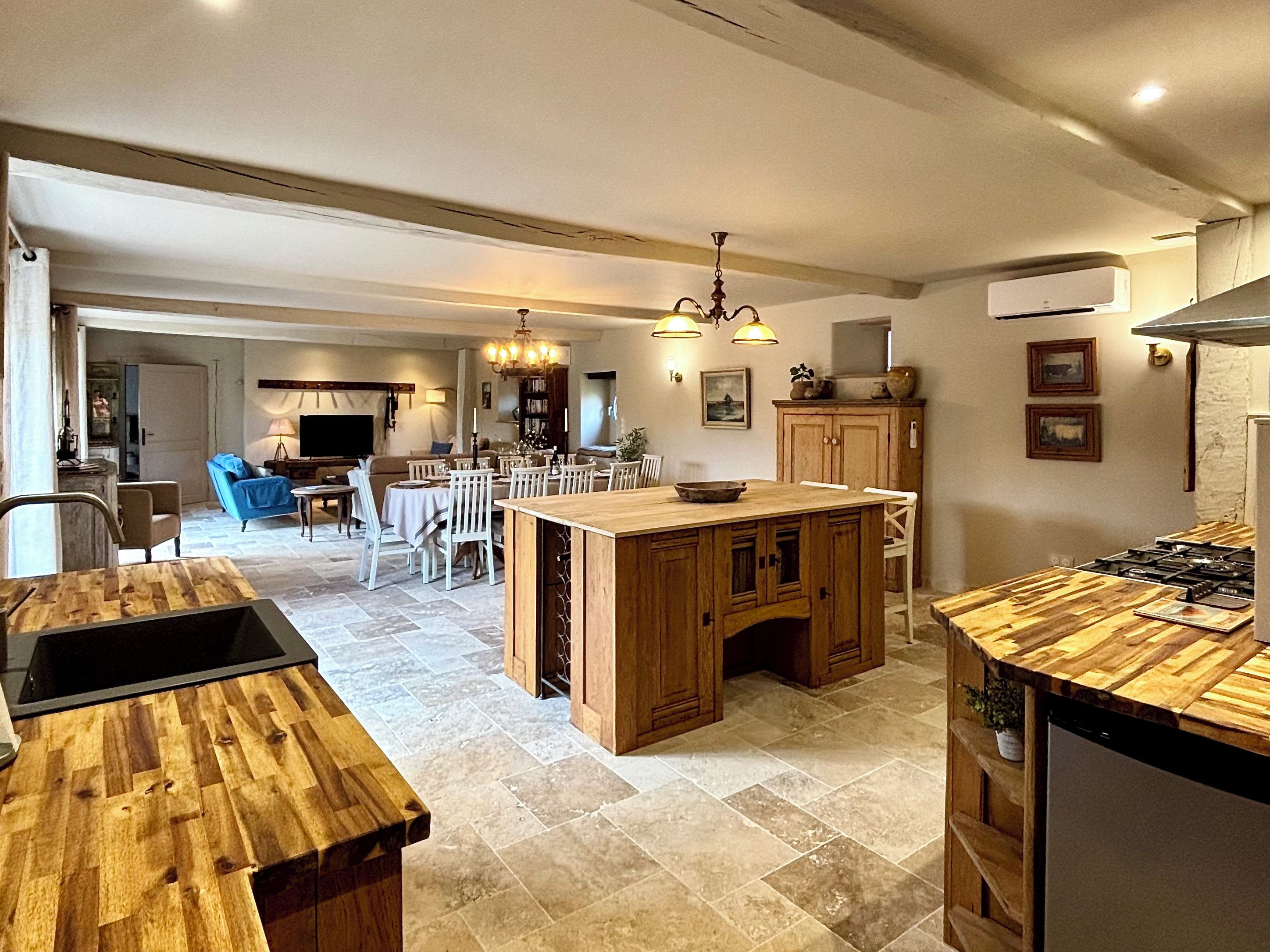A spacious kitchen with a central island, dining area, and a living room with a sofa and TV.