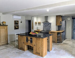 A modern kitchen with wooden cabinets, a central island, a stove, and a refrigerator. - Luxury chateau retreat; pool, summer kitchen, outdoor cinema & Madiran vineyards (Castelnau-Rivière-Basse)