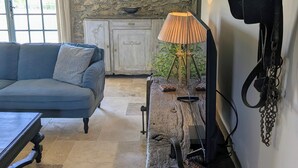 Et værelse med en blå sofa, en træbænk med magasiner, en lampe, en stenvæg, et vindue med en gyngende hest og et hvidt skab.