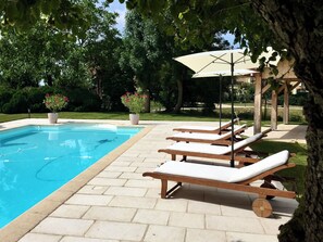 A swimming pool with lounge chairs and a pergola with an umbrella. - Luxury chateau retreat; pool, summer kitchen, outdoor cinema & Madiran vineyards (Castelnau-Rivière-Basse)