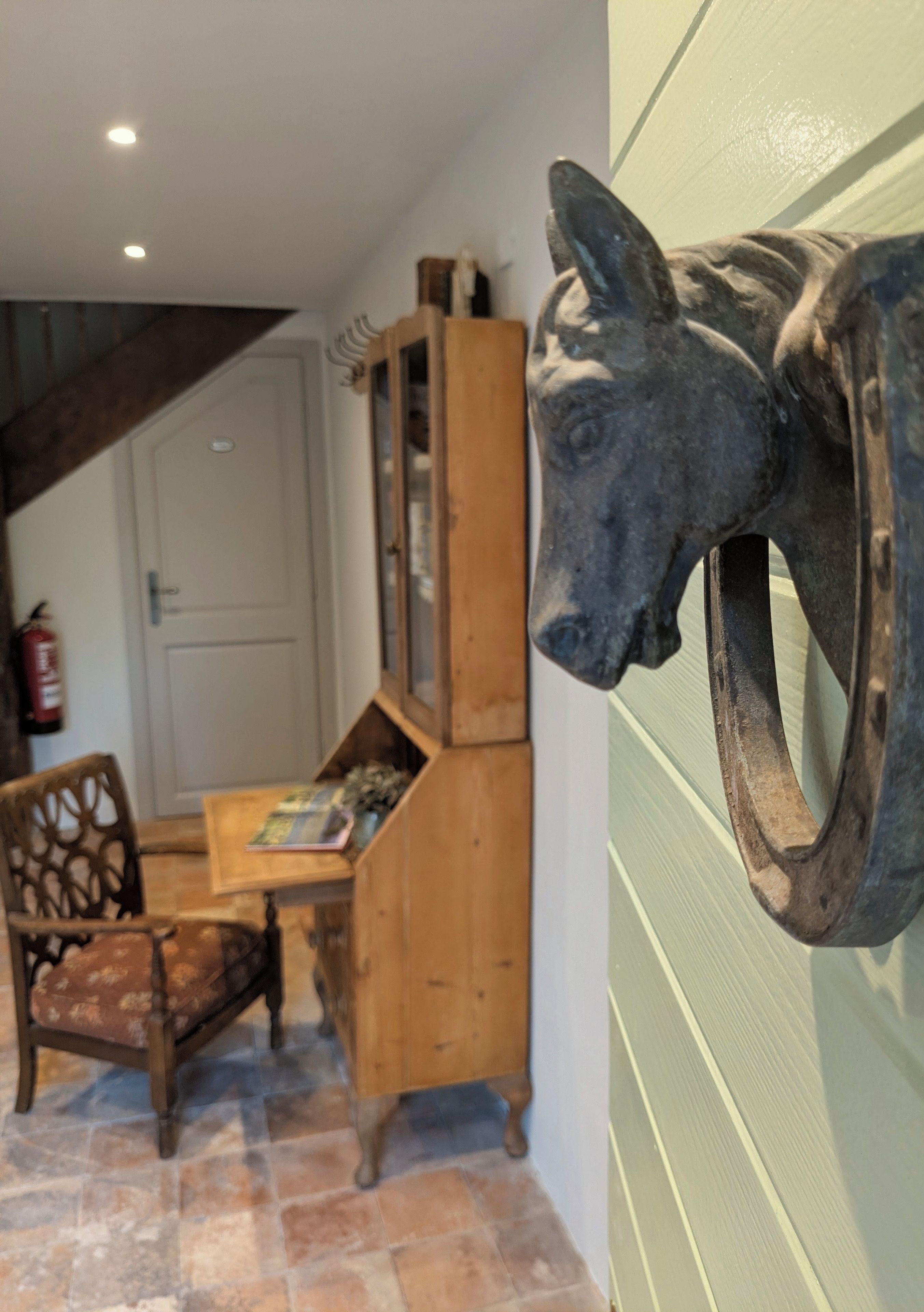Een kamer met een houten bureau, een stoel, een boekenkast en een sculptuur aan de muur.