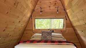 A cozy attic bedroom with a bed, a window, and a cowhide rug. - White Mountains A-Frame | Off-Grid, Stars, Firepit (Stoneham)