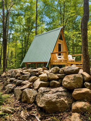 Une cabane avec un toit en pente, un revêtement extérieur en bois et une véranda avec des chaises.