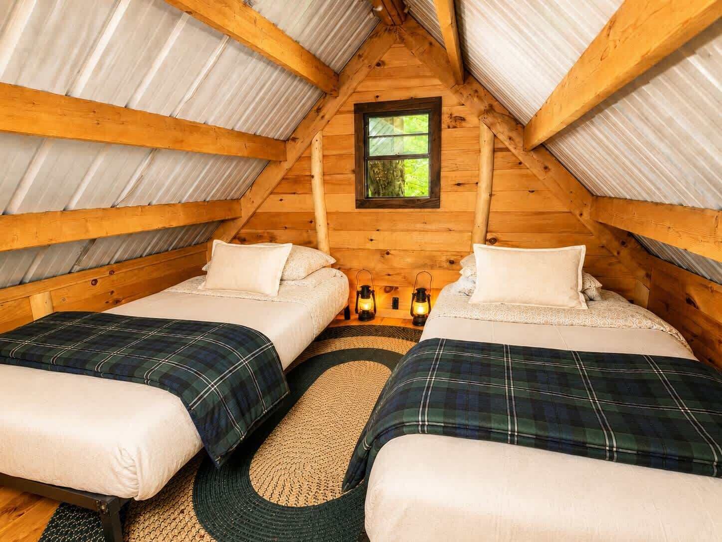 A cozy attic bedroom with two beds, a window, and lanterns.
