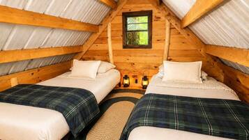 A cozy attic bedroom with two beds, a window, and lanterns.