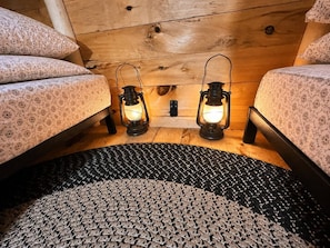 A cozy room with two beds, a patterned rug, and two lit lanterns. - Off-Grid Treehouse! White Mountain National Forest (Stoneham)