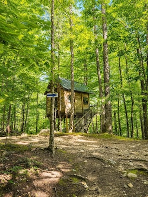 A wooden cabin elevated on stilts in a forest, with a sign indicating a direction. - Off-Grid Treehouse! White Mountain National Forest (Stoneham)