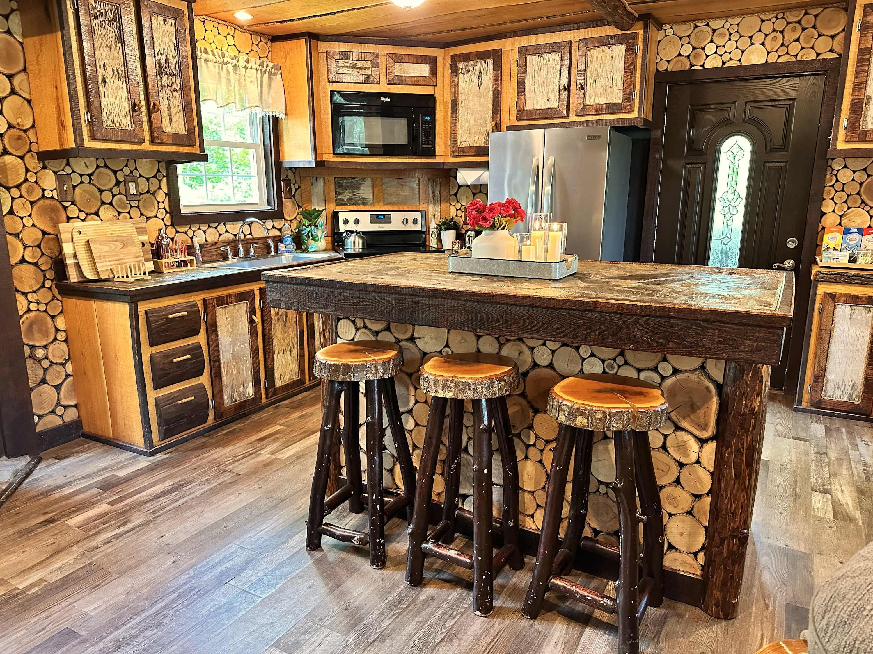 Una cocina rústica con una isla central, taburetes de madera y un fondo de pared de piedra.