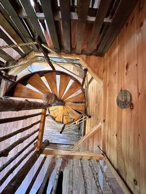 A wooden spiral staircase with a rustic design, featuring a wooden handrail and a central wooden wheel.