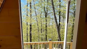 Um deck de madeira com guarda-corpo de metal, um banco azul e vista clara para uma área arborizada.