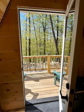 A wooden deck with a metal railing, a blue bench, and a clear view of a forested area.