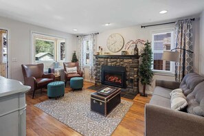 Ein Wohnzimmer mit Kamin, Ledersesseln, Poufs, einer Couch und einem Teppich.