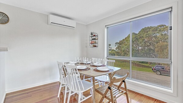 A dining area with a large window, white walls, and a view of a car on the road.